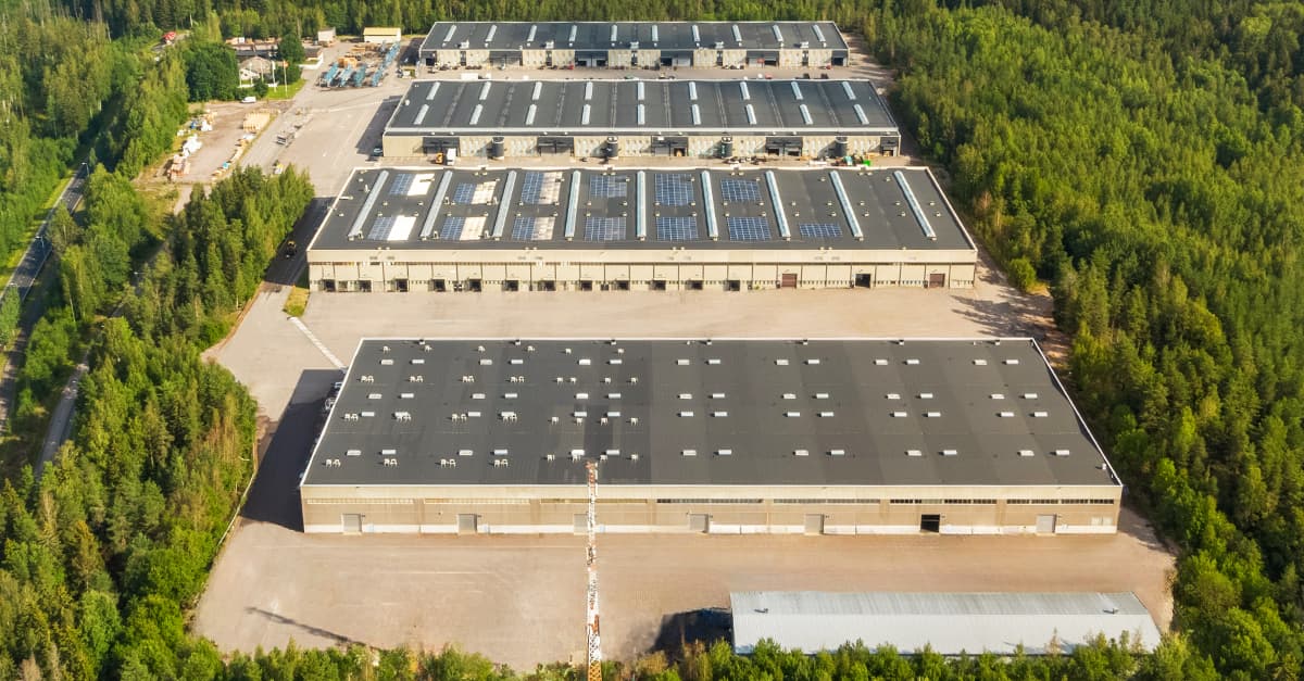 Aerial view of large industrial warehouses surrounded by dense green forest.