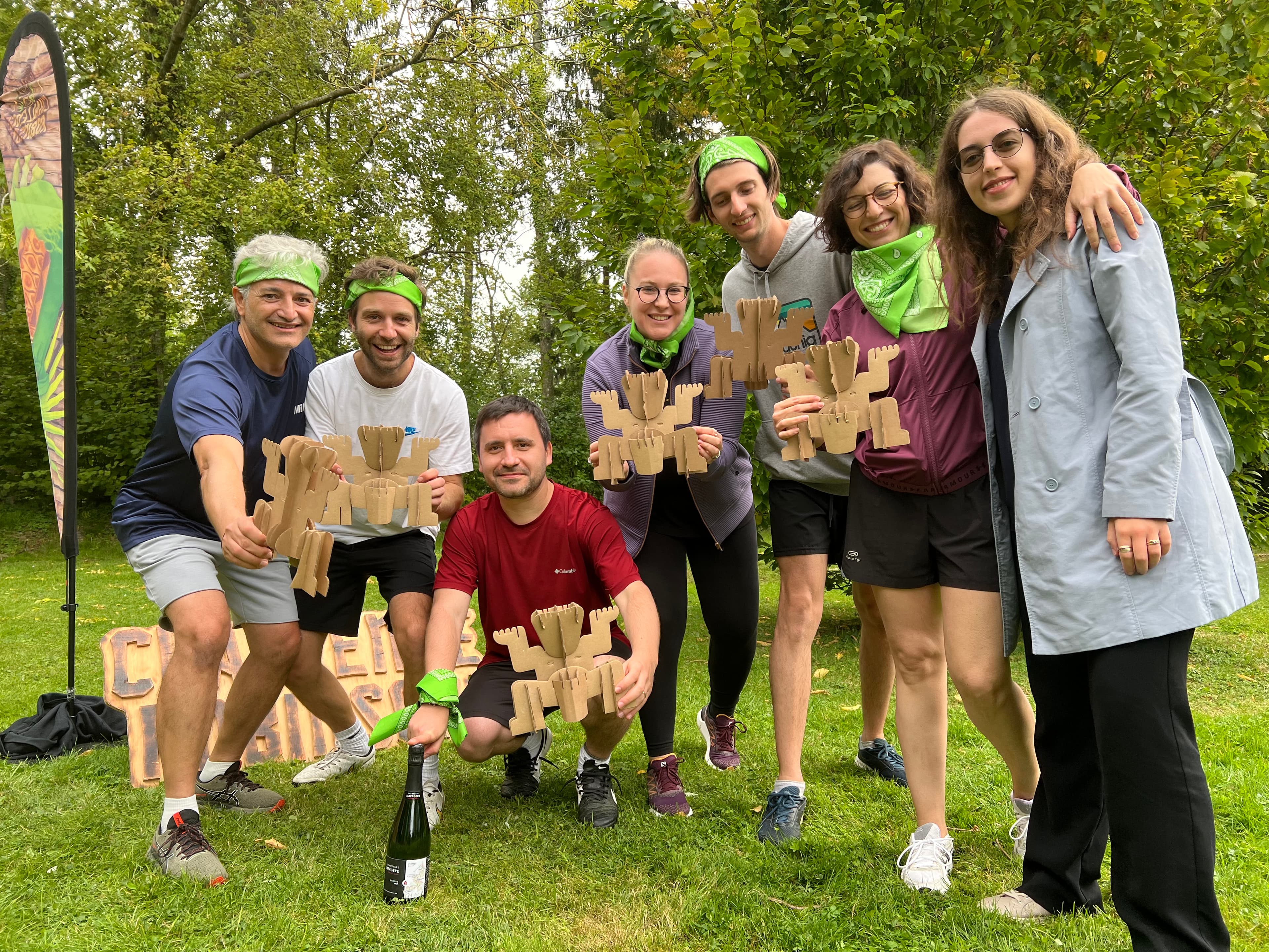 A group of people outdoors holding wooden plaques and wearing green bandanas, with trees in the background.