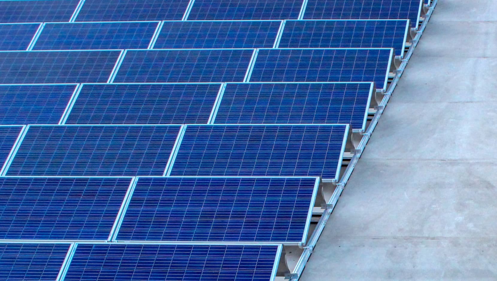 Filas de paneles solares azules instalados sobre una superficie plana y de color claro.