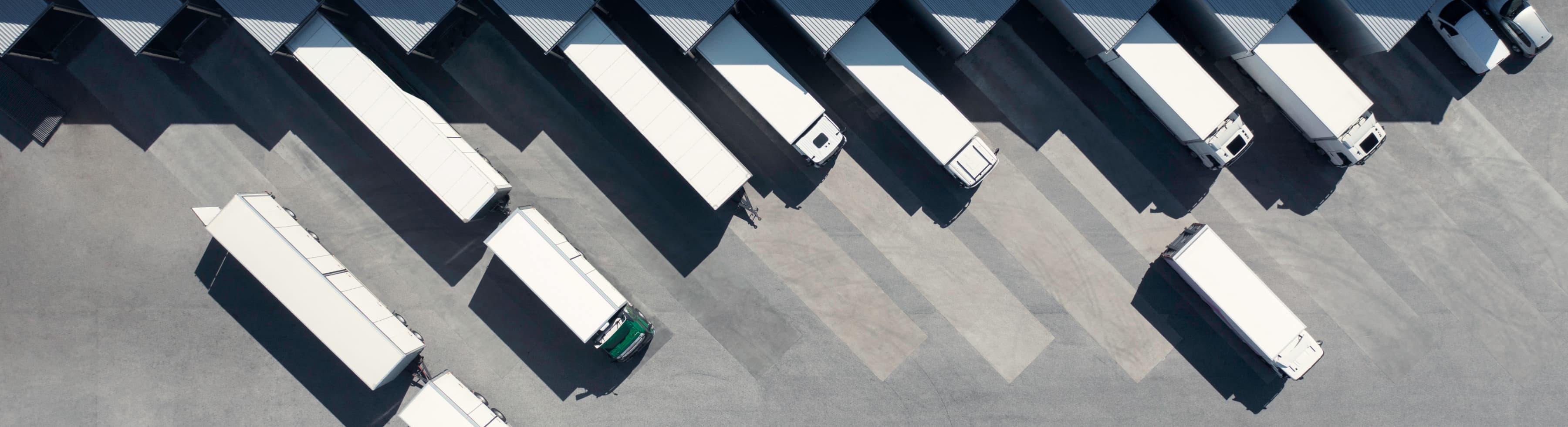 Aerial view of trucks parked at loading bays, with shadows cast on the ground.