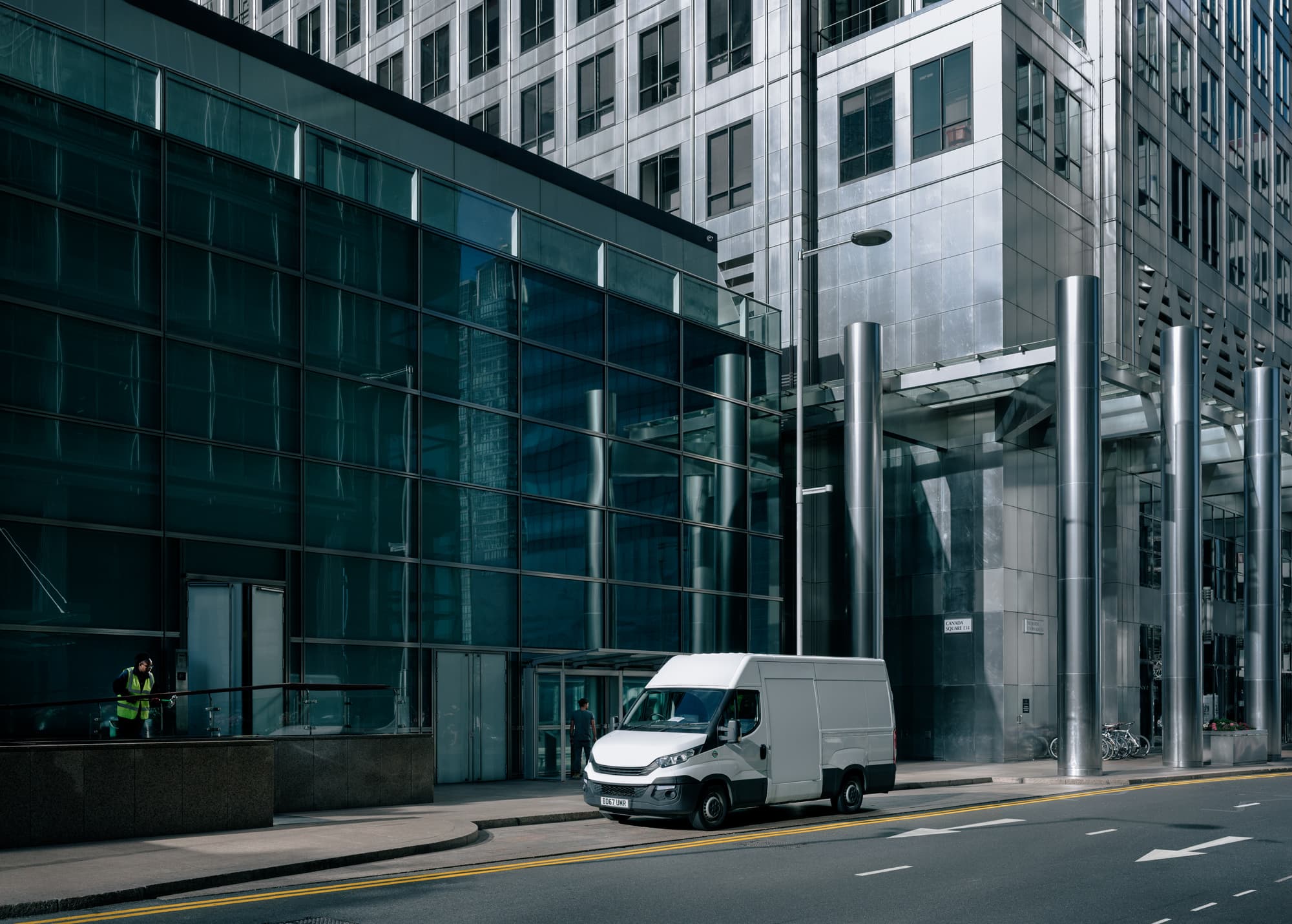 A white delivery van parked on the street beside a modern glass and steel office building.