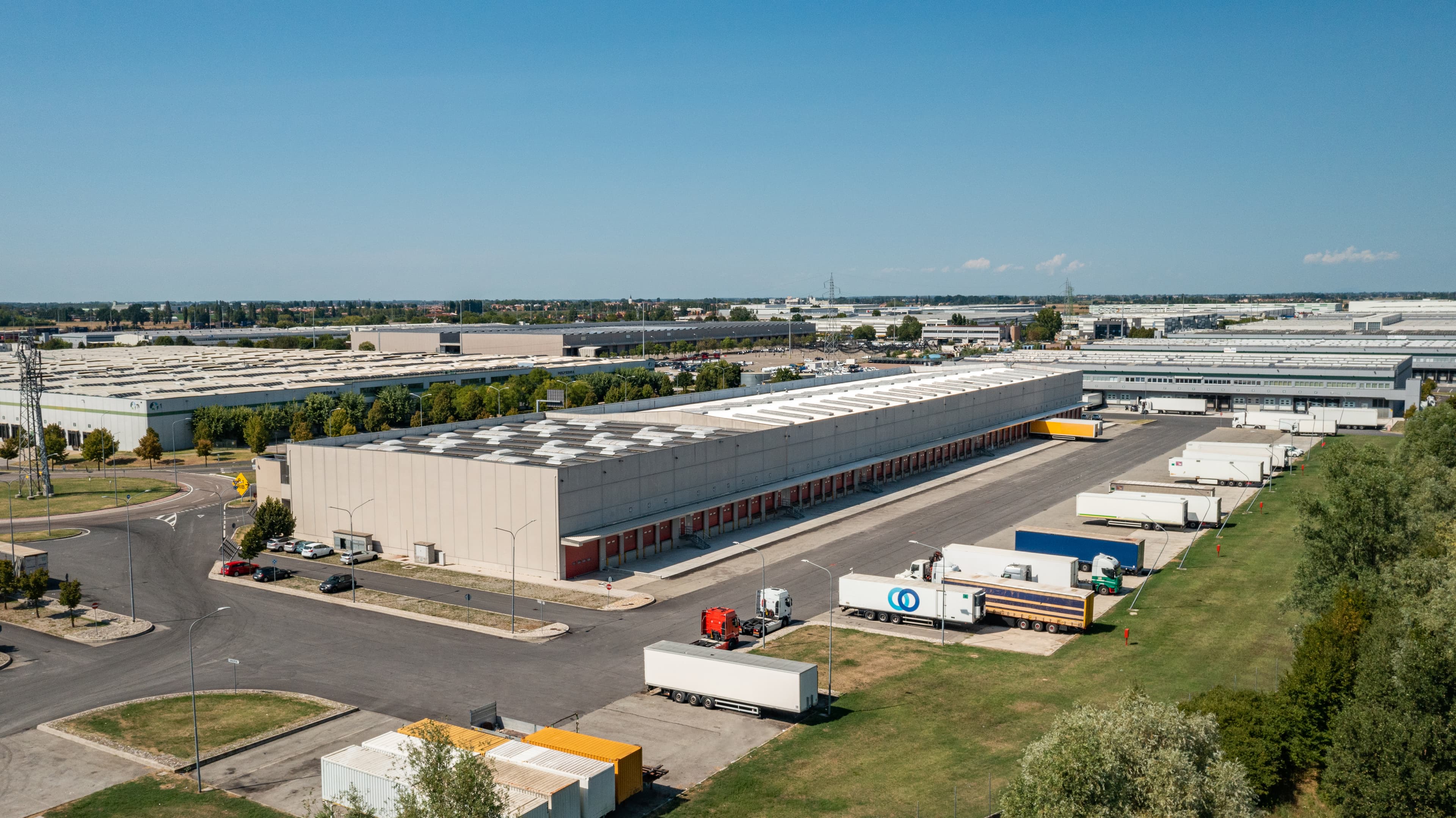 Aerial view of a large industrial complex with warehouses, loading docks, and several parked trucks on a clear day.