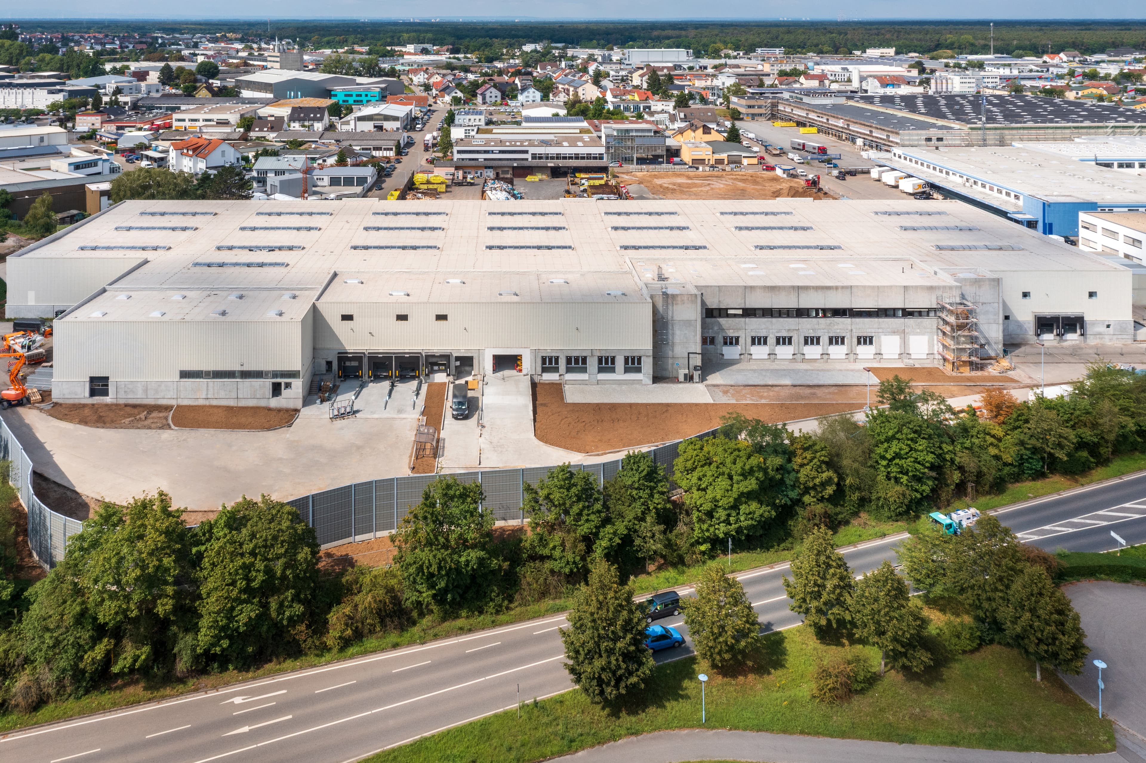Aerial view of a large industrial warehouse complex with multiple loading docks, surrounded by roads and greenery.