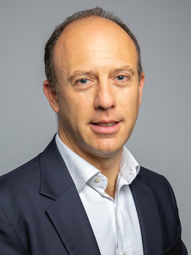 A person in a business suit is looking at the camera against a plain background.