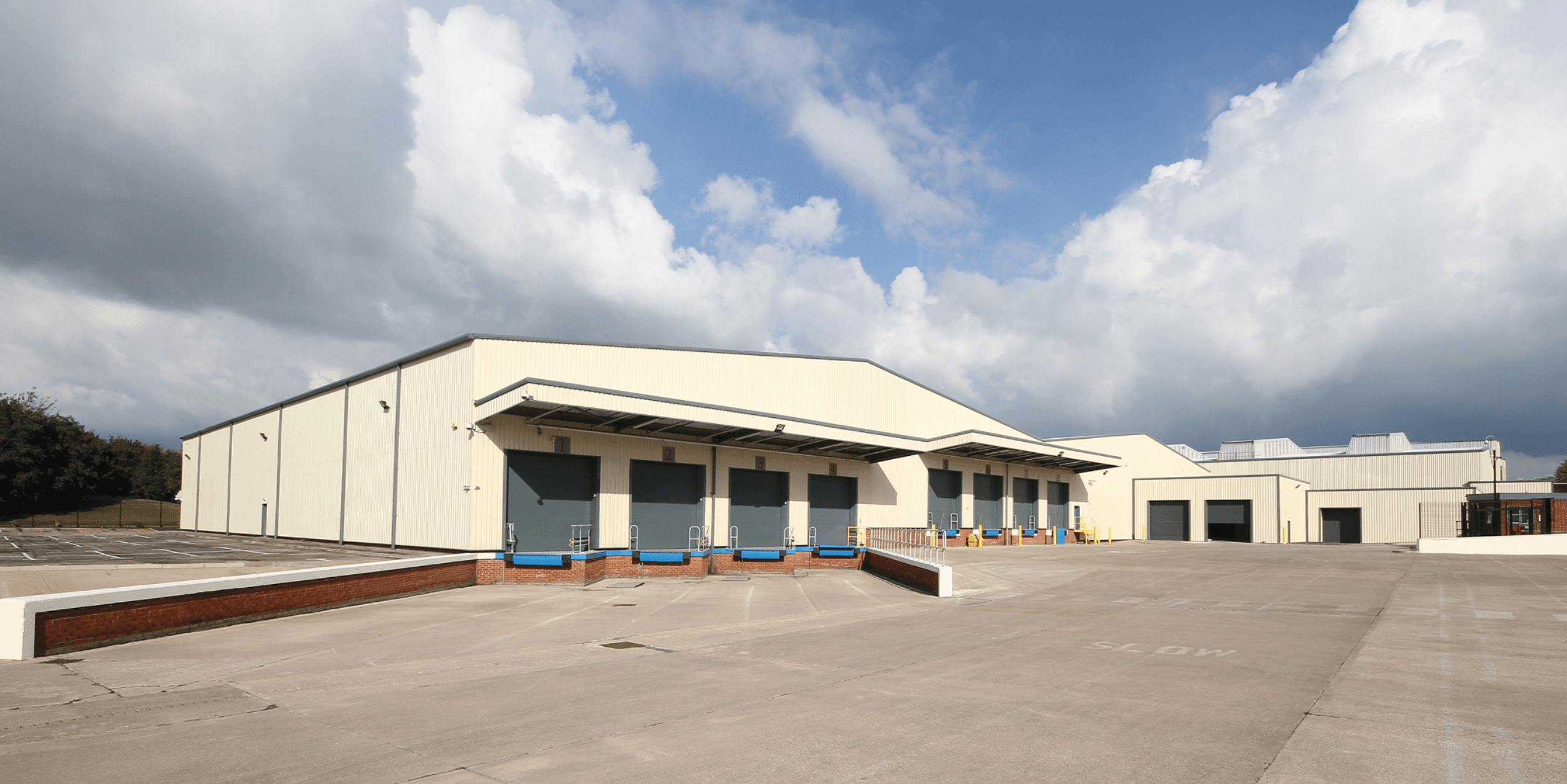 Large industrial warehouse with multiple loading docks, set on a spacious concrete lot under a partly cloudy sky.
