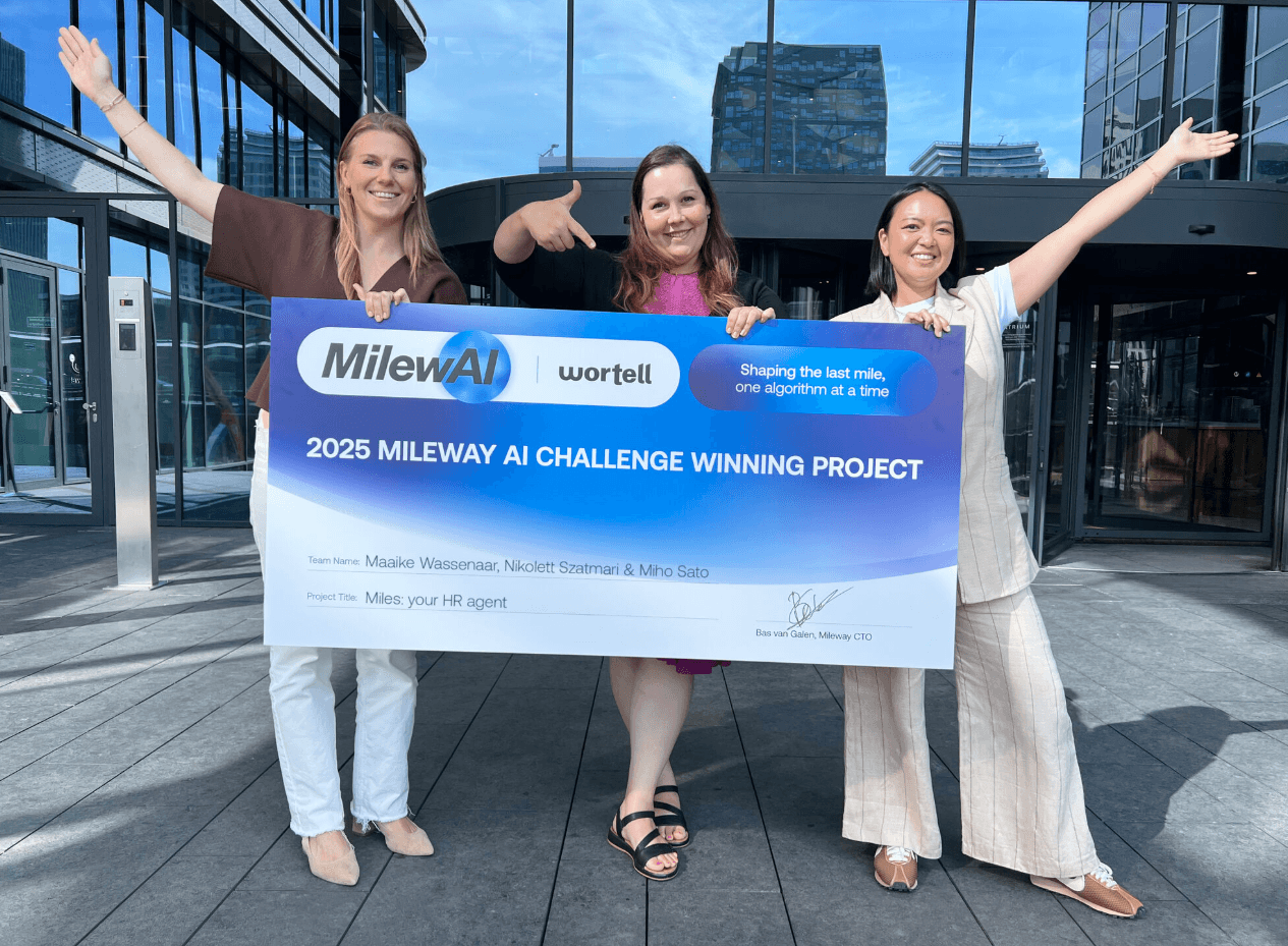 Three women stand outside a modern building, holding a large banner announcing their 2025 Mileway AI Challenge winning project.